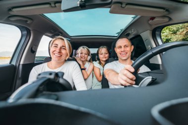 Otomobil kazasında iki kızı olan mutlu genç bir çift. Yolculuk sırasında gülümsüyorlar, gülüyorlar. Aile değerleri, seyahat kavramları.