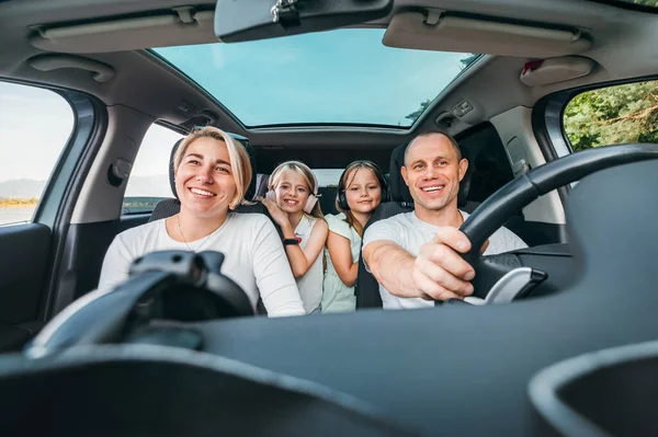 自動車の熱帯の間に車の中に2人の娘と幸せな若いカップル 笑顔で 旅の途中で笑っている 家族の価値観 旅行コンセプト — ストック写真