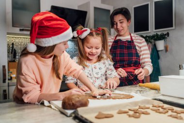 Kırmızı Noel Baba şapkalı şirin kızlar ve ev yapımı ev yapımı zencefilli kurabiye kurabiyeleri yapıyorlar. Ev mutfağında kurabiye keskisi kullanıyorlar. Mutlu aile tatili hazırlıkları, çocukluk konsepti.