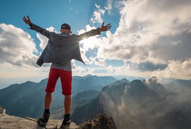 Rysy Zirvesi 249m 'de ayakta duran ve sabah erken saatlerde inanılmaz bir ışık ve gölgelerle kaplı bulutlarla kaplı High Tatras sıradağlarının tadını çıkaran bir gezgin. Doğa, yürüyüş, tırmanma.