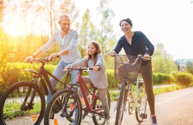 Yazın bisiklet sürerken kızıyla birlikte gülümseyen anne ve baba. Onlar yaz şehir parkında birliktelikten hoşlanırlar. Mutlu ebeveynlik ve çocukluk veya aktif spor hayatı konsepti imajı.