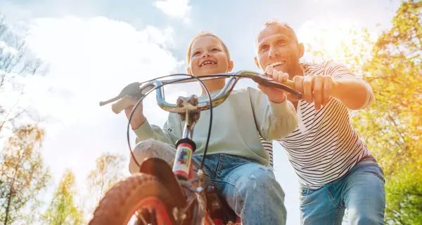 笑顔の父は自転車に乗るように娘に教える 彼らは夏の都市公園で一緒に楽しむ 幸せな子供の頃のコンセプト低角度ショット画像 — ストック写真