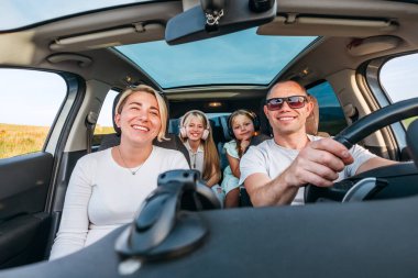Otomobil kazası sırasında arabada iki kızı olan mutlu genç bir çift. Onlar bir yolculuk sırasında gülümsüyor ve gülüyorlar. Aile değerleri, seyahat kavramları.