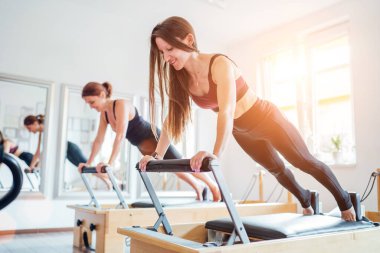 Spor spor salonundaki pilates reformatör spor aletini kullanarak uzun tahta statik kas güçlendirme egzersizi yapan iki genç bayan. Aktif insanlar eğitim, yoga dersleri konsepti.