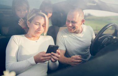 Otomobil kazası sırasında arabadaki arka koltuklarda iki kızı olan mutlu genç çift. Akıllı telefon kullanarak bir araba rotasını arıyorlar. Aile değerleri, seyahat, sosyal medya ve yeni teknoloji kavramları.