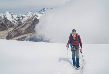 Sırt çantalı, güneş gözlüklü gülen dağcı 6000 metre yükseklikteki Mera zirvesinden yükselen sırıkla efsanevi Everest, Nuptse, Güney Yüzlü Lhotse duvarlı güzel Yüksek Himalayalar 'ın keyfini çıkarıyor..