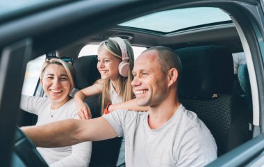 Happy young couple with daughter inside the modern car with panoramic roof during auto trop. They are smiling, laughing during road trip. Family values, traveling concepts.	