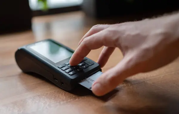 Man palm typing POS terminal buttons pin-code credit doing wireless bank payment with process acquire at table cafe restaurant indoor. Focus on machine. Finance, restaurant industry, small business.