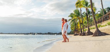 Couple in love hugging on sandy exotic beach while having evening walk by Trou-aux-Biches seashore on Mauritius island enjoying sunset. People relationship and tropic honeymoon vacations concept image clipart