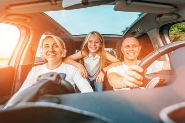 Otomobil kazası sırasında panoramik çatısı olan modern arabanın içinde kızı olan mutlu genç bir çift. Yolculuk sırasında gülümsüyorlar, gülüyorlar. Aile değerleri, seyahat kavramları.