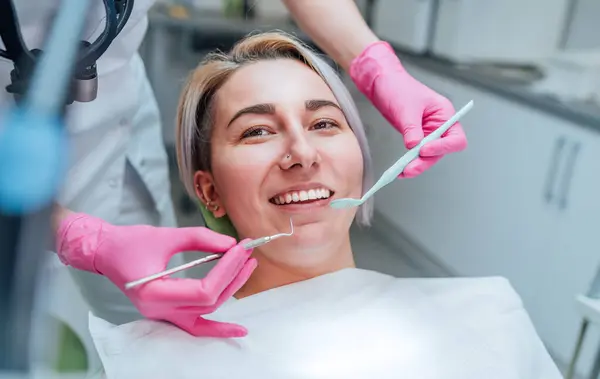在口腔科诊所的椅子上 坐在医生的手上 手持口镜和牙科探测工具准备检查牙齿状况的年轻微笑妇女的画像 保健概念 — 图库照片