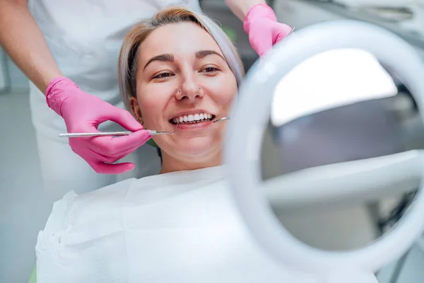 用挖掘机和镜像医疗工具对着口腔科椅子中的镜子和粉色手套中优雅的牙医手掌微笑的女性画像 医疗保健和医疗行业概念形象 — 图库照片