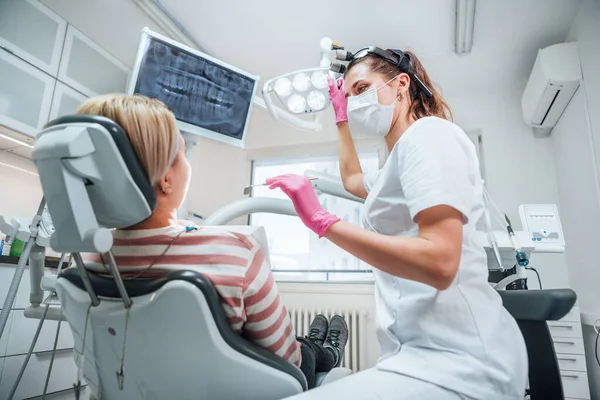 牙科诊所的病人去现代医务室看病 牙医女医生穿着制服 戴着放大镜 指明方向 病人坐在椅子上 医疗保健和医疗行业概念形象 — 图库照片