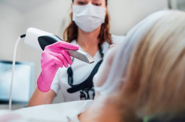 Üniformalı dişçi kadın doktor, düzgün hizalayıcı üretimi için intraoral üç boyutlu diş tarayıcı makinesi kullanıyor. Dişçi kliniğindeki hasta modern sağlık koğuşunu ziyaret ediyor. Sağlık dişleri, sağlık sektörü konsepti.