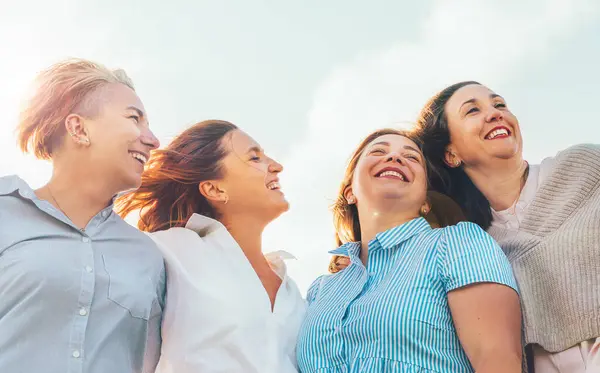 Gün batımında yeşil tepenin yanında yürürken gülümseyen ve gülen dört kadının portresi. Kadınların dostluğu, ilişkileri ve mutluluk konsepti imajı.