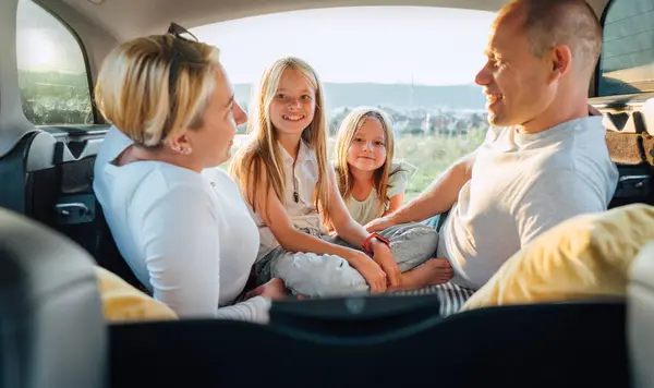 笑顔の小さな姉妹の肖像画 自動車トロフィーの間に車のトランクの中の2人の娘と幸せな若いカップル 笑ったり 笑ったり しゃべったりしている 家族の価値観 旅行コンセプト — ストック写真
