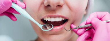 Stomatoloji sandalyesinde oturan gülümseyen orta yaşlı kadın portresi ve kazıcı ve ayna tıbbi aletleriyle pembe eldivenli zarif dişçi avuçları. Sağlık ve sağlık sektörü konsepti