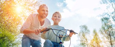 Gülümseyen baba kızına bisiklet sürmeyi öğretiyor. Onlar yaz şehir parkında birliktelikten hoşlanırlar. Mutlu çocukluk konsepti düşük açı görüntü.