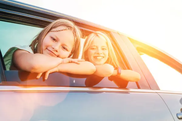 2人の幸せな姉妹が自動車旅行中に車の窓を開けている かわいい女の子は笑って 道のジョーニーの間を笑っている 家族の価値観 旅行コンセプトサイドカービュー写真 ストック写真