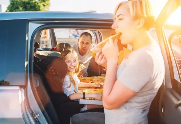 子供の車の座席で積極的な笑顔の女の子一方 家族の車の旅ブレーキだけでイタリアのピザを調理食べて停止します 幸せな家族の瞬間 子供時代 ファーストフードや自動車旅行のランチ休憩のコンセプトイメージ ロイヤリティフリーのストック画像