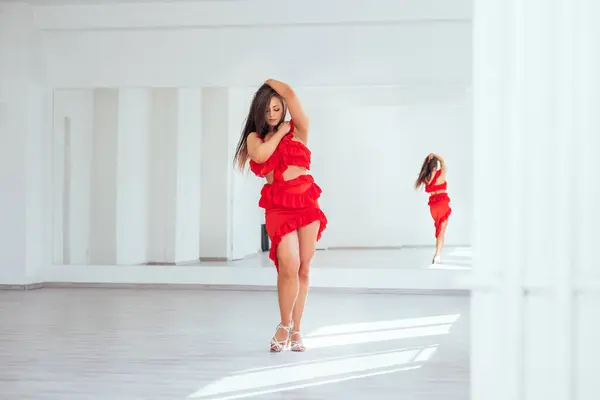 优雅的女人穿着红色拉丁舞衣 穿着雅致的舞步 穿着白色的大厅堂和大镜子墙 人们在舞蹈中的表现 女性的美体观念形象 — 图库照片