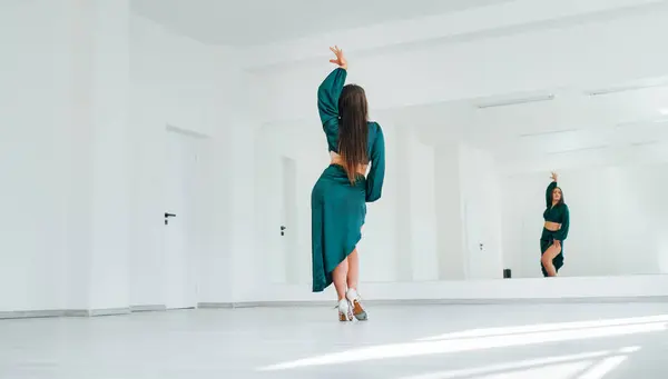 优雅的女人穿着深绿色的拉丁舞衣 穿着雅致的舞步 穿着白色的大厅堂和大镜子墙 人们在舞蹈中的表现 女性的美体观念形象 — 图库照片