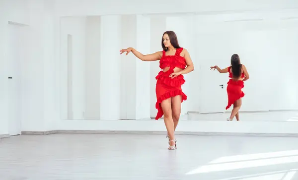 赤いラテンダンスのドレスを着た優雅な女性は 大きな鏡の壁で白い色の大きなホールでエレガントなダンスの動きをする ダンス中の人々の表情 女性の身体コンセプトイメージの美しさ ストック画像