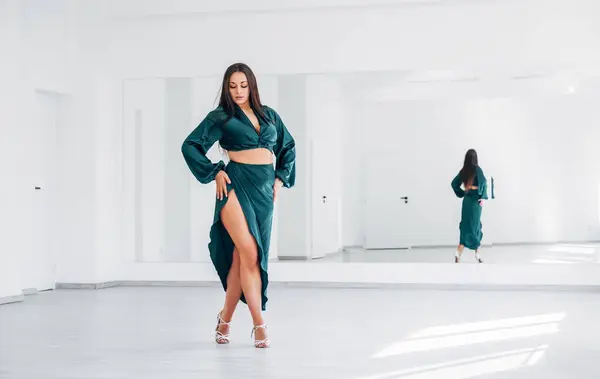 优雅的女人穿着深绿色的拉丁舞衣 在白色的大大厅里跳着优雅的舞步 有一面大镜子墙 人们在舞蹈美的过程中的表现 女性的身体概念形象 图库图片
