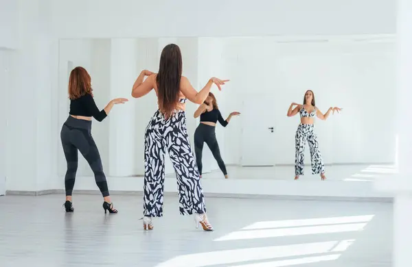 Graceful dancing women group doing elegant dance movements in white color spacious hall with big mirror wall.People\'s expressions during dancing, beauty of woman\'s body, active lifestyle concept image