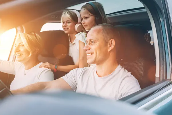 自動車の熱帯の間に車の中で2人の娘と一緒に笑顔の若いカップル 笑顔で 旅の途中で笑っている 家族の価値 自動車産業のコンセプト ロイヤリティフリーのストック写真