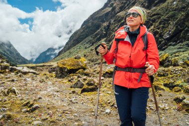 Portrait of Woman in sunglasses with backpack and trekking poles dressed red softshell jacket hiking on Makalu Barun National Park trek in Nepal. Mountain hiking, traveling and active people concept clipart
