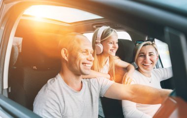 Happy young couple with daughter inside the modern car with panoramic roof during auto trop. They are smiling, laughing during road trip. Family values, traveling concepts.	