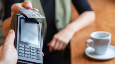 Kablosuz banka ödemesi yapan genç bir kadın POS terminal işlemleri ile birlikte kapalı kafeterya restoranından satın alınıyor. Makineye odaklan. Finans, restoran endüstrisi, küçük işletmeler.