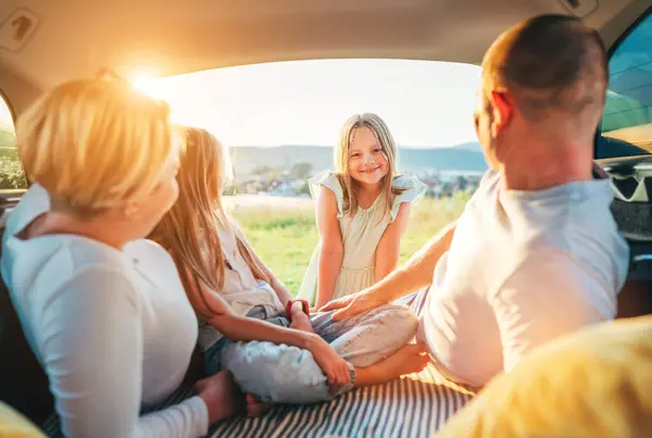 カメラを見つめている幸せな笑顔の少女の肖像 自動車トロフィーの間に車のトランクの中の2人の娘と幸せな若いカップル 彼らは笑って チャットする 家族の価値観 旅行コンセプト ロイヤリティフリーのストック画像