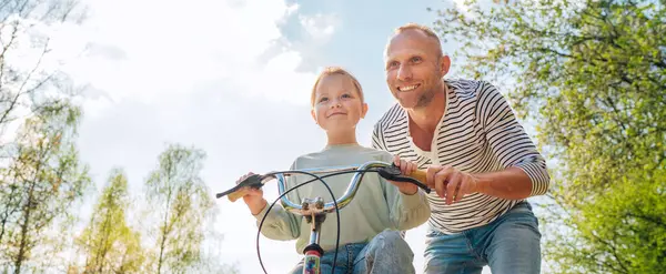 笑顔の父は自転車に乗るように娘に教える 彼らは夏の都市公園で一緒に楽しむ 幸せな子供の頃のコンセプト低角度ショット画像 ストックフォト