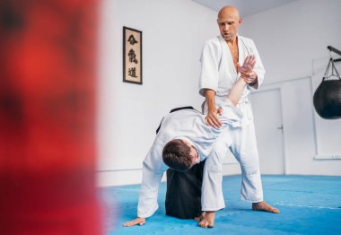 İki adam Aikido 'da aikido antrenmanı yapıyor. İkisi de Japon kanji AIKIDO sözcüğünün yer aldığı geleneksel dövüş sanatları kimonosu ve Hakama giyiyorlar.