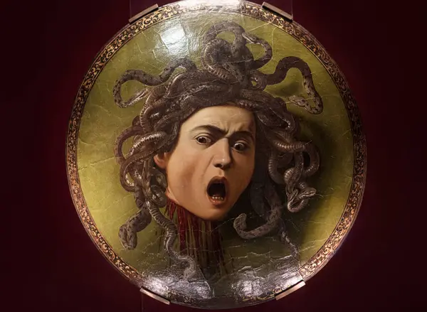 stock image Florence, Italy - May 23, 2023: Famous Painting masterpiece of Medusas head with snakes hair, mouth agape in terror, displayed on a round shield by Baroque painter Caravaggio in Uffizi Gallery, Italy.