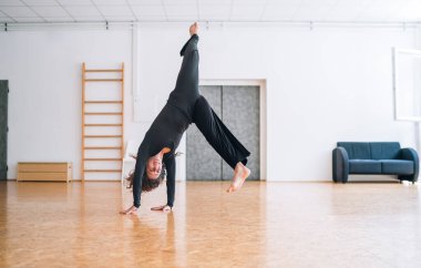 Modern akrobatik dansçı, parlak dans stüdyosunda etkileyici bir amuda kalkarak güç ve esneklik sergiliyor. Onun dinamik hareketi ve odak noktası sanatsallığı, çağdaş dans atletizmi