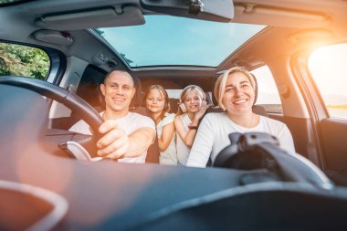 Otomobil kazasında iki kızı olan mutlu genç bir çift. Yolculuk sırasında gülümsüyorlar, gülüyorlar. Aile değerleri, seyahat kavramları.