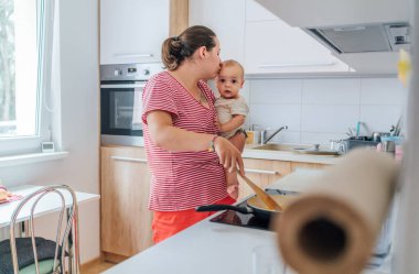 Anne, bebeğine sıcak bir mutfakta yemek hazırlıyor. Şefkatli bir bakım ve bağ kurma anı. Kadın doğum izninde ve oğlunun birlikteliğinden zevk alıyor.. 