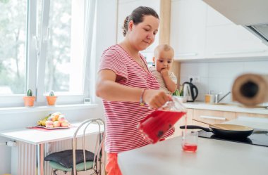 Anne, bebeğine sıcak bir mutfakta yemek hazırlıyor. Şefkatli bir bakım ve bağ kurma anı. Kadın doğum izninde ve oğlunun birlikteliğinden zevk alıyor.. 