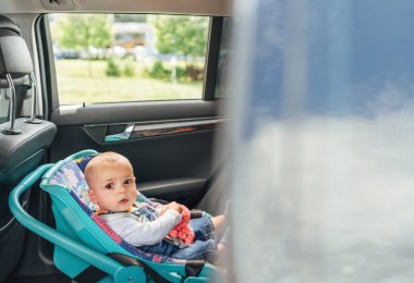 Bebek güvenli bir şekilde bebek koltuğuna oturmuş, pencereden dışarı bakıyor. Arabanın içi geniş ve dışarısı yeşil park gibi görünüyor. Bu görüntü seyahat güvenliğinin ve çocukluğun masumiyetini yakalar.