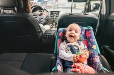Annem yolcu arabası kullanırken bebek koltuğunda gülmenin portresi. Sahne, otomobil yolculuğu sırasında çocuk güvenliğinin önemini vurgulayan bakım ve sorumluluk anını yakalar.