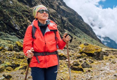 Nepal 'de Makalu Barun Ulusal Parkı' nda yürüyüş yaparken sırt çantalı ve yürüyüş direkleri takmış kırmızı yumuşak kabuklu kadın portresi. Dağ yürüyüşü, seyahat ve aktif insanlar konsepti