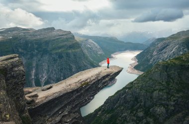 Kadın yürüyüşçü parlak kırmızı ceket giyip ünlü Trolltunga 