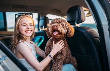 Portre Fluffy kahverengi Maltipoo köpeği ve küçük kız portresi onlar araba yolculuğu sırasında arka koltukta otururken. Modern bir aile kavramında komik hayvanlar.