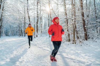 Güneşli, karlı bir günde karlı ormanda koşan parlak rüzgarsız ceketler giyen genç çiftler. Sportif insanlar, kış eğitimi ve akrabaların konsept imajı