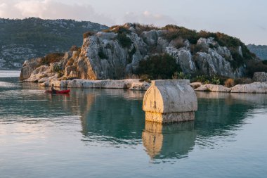 Türkiye 'nin antik Simena Kaleky kentinden taş lahit Akdeniz' in berrak sularına kısmen batmış ve sabah ışığı listelenmiş engebeli tepelerle çevrili bulunuyor. Lycia 'nın arkeolojik hazinesi