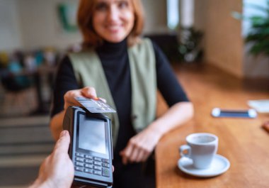 Kablosuz banka ödemesi yapan genç bir kadın POS terminal işlemleri ile birlikte kapalı kafeterya restoranından satın alınıyor. Makineye odaklan. Finans, restoran endüstrisi, küçük işletmeler.