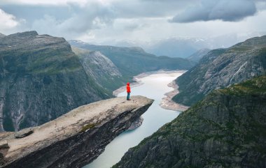Kadın yürüyüşçü parlak kırmızı ceket giyip ünlü Trolltunga 